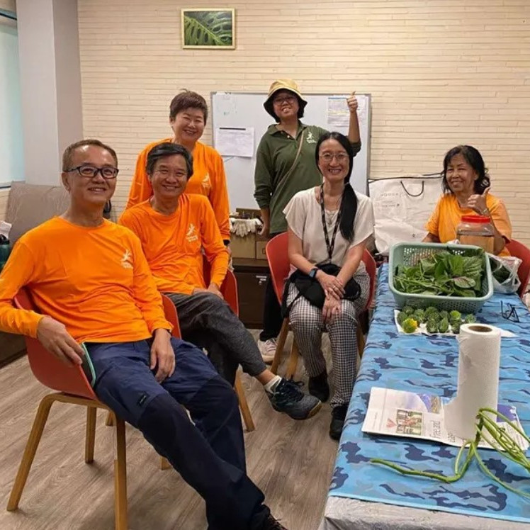 A group of people in orange shirts gathered around a table adorned with plants, engaged in conversation